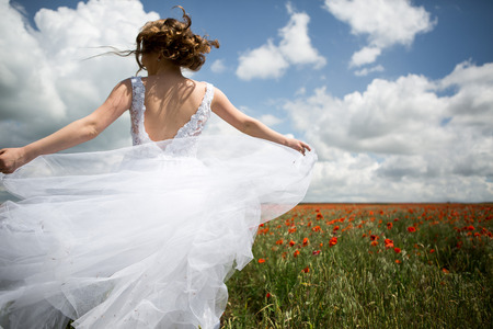 Bride running on a field of blooming poppies in a wedding dress.の写真素材