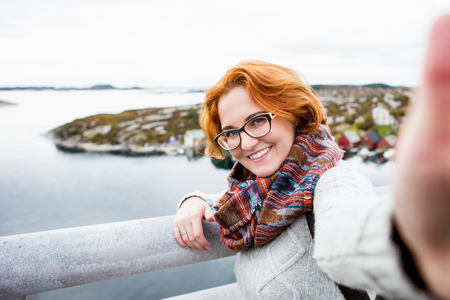 Red-haired girl with glasses makes selfie on background of ocean and islands.の写真素材