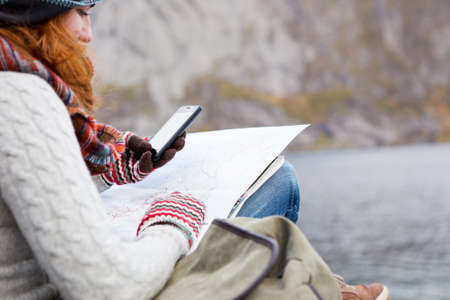 Woman traveler with a backpack, map and phone sitting on a wooden pier.の写真素材