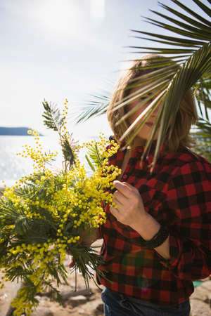 Portrait of a woman holding a bouquet of mimosa flowers. The girl on the beach. A woman is dressed...