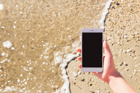 A woman is holding a phone against a sea beach. Blank screenの写真素材