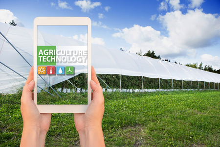 A farmer holding a tablet on the background of the greenhouse. On the screen, the inscription...