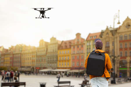 A man with a backpack controls a drone on a background of a European city