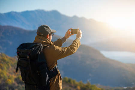 Traveler with a backpack and a smartphone stands on a mountain