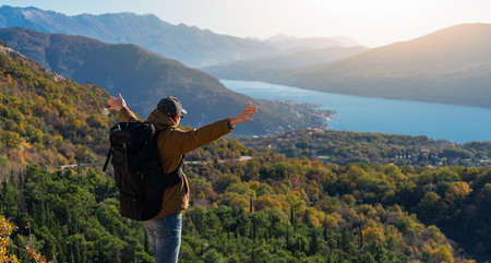 A traveler with a backpack stands on the top of the mountain