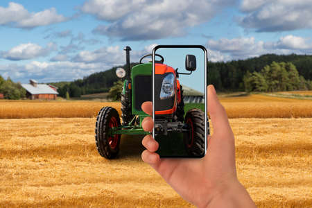 Old tractor on the farm. The farmer points his phone at this and a new modern tractor is shown on...
