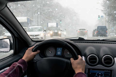 A man drives a car on a winter city in a blizzardの写真素材