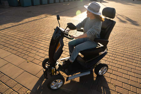 Woman tourist riding a four wheel mobility electric scooter on a city street.
