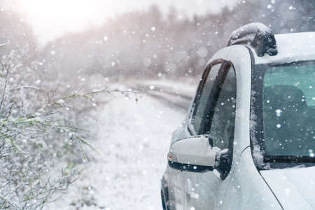 White car on a winter road through a snow covered forest.