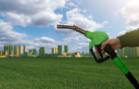Hand with fuel nozzle with inscription BIO on the background of green eco city. Biofuel conceptの写真素材