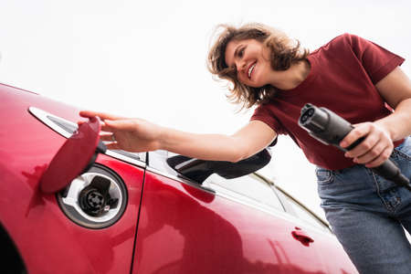 Woman holds a charging plug for an electric car and opens the charging hatchの写真素材