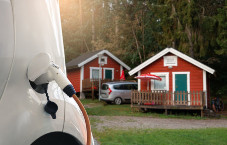Close-up of a charging cable connected to an electric car against the backdrop of a campsiteの写真素材