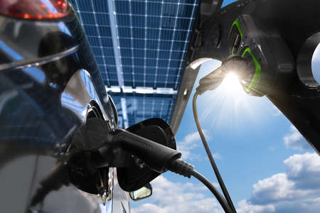 Electric car is charged from a charging station at carport that takes energy from solar panels. close upの写真素材