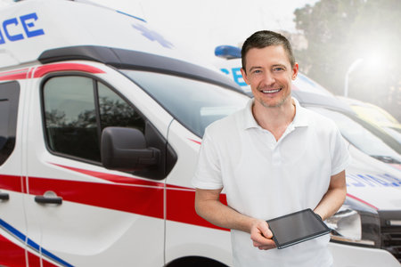 Male doctor with a digital tablet smiling and looking at the camera on the background of ambulanceの写真素材