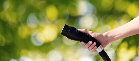 Hand with charger plug for electric car on a green background