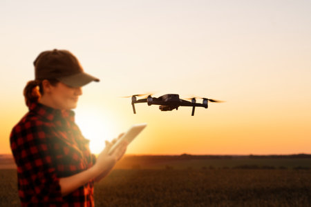 Farmer controls drone sprayer with a tablet on a sunset. Smart farming and precision agricultureの写真素材