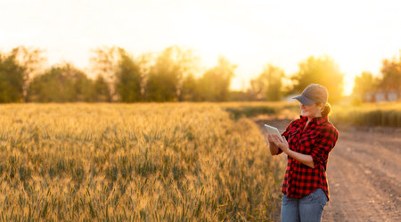 A woman farmer examines the field of cereals and sends data to the cloud from the tablet. Smart...