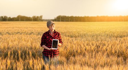 A woman farmer examines the field of cereals and sends data to the cloud from the tablet. Smart...