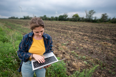 Farmer with laptop on the field. Wind turbines on a horizon. Smart sustainable farming and...