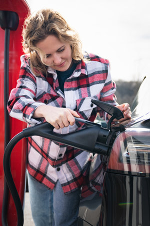 Woman in a plaid shirt charging an electric car. High quality photoの写真素材