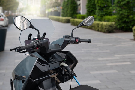 Electric scooter with connected charging cable on a city street. High quality photo