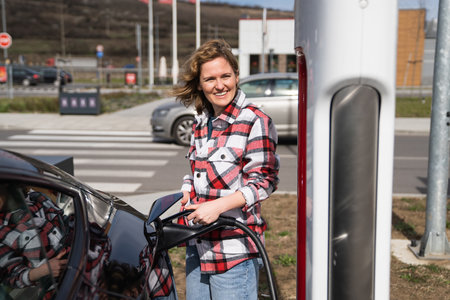 Woman in a plaid shirt charging an electric carの写真素材