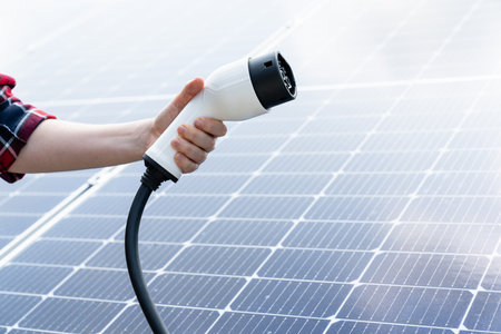 Hand with electric vehicles charging plug on a background of solar panelの写真素材