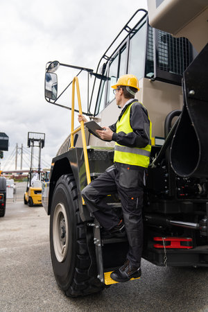 Engineer with tablet computer stands on the stairs to the cab of a truck.