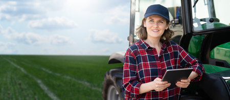 Woman farmer with a digital tablet next to agricultural tractorの写真素材