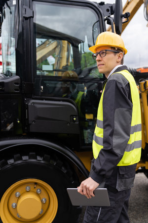 Engineer in a helmet with a digital tablet next to construction excavators