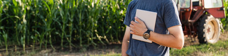 Farmer with a digital tablet is next to an agricultural tractor..