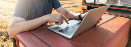 Farmer works on laptop next to an agricultural tractor.の写真素材