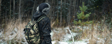 Male hunter in camouflage and with backpack, armed with a rifle, walks through the snowy winter forest..の写真素材