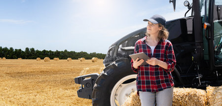 Woman farmer with a digital tablet next to agricultural tractor.の写真素材