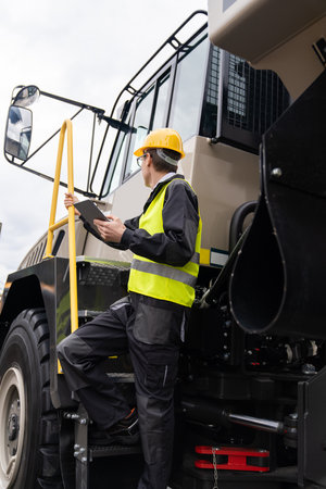 Engineer with tablet computer stands on the stairs to the cab of a truck.