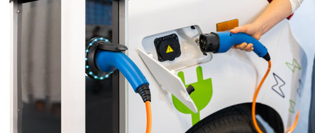 Woman holding plug of electric car charging station.
