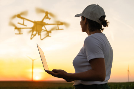 Woman farmer wearing white cap and t-shirt with laptop. Wind turbines in the background.