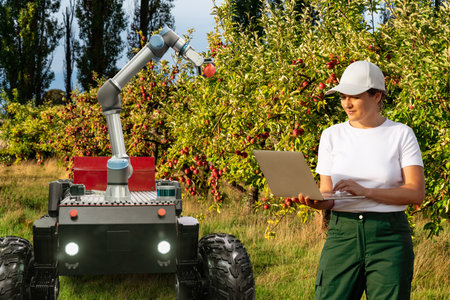 Farmer controls autonomous robot harvester with robotic arm harvesting apples on a smart farm. Concept..の写真素材