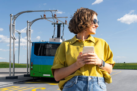 Woman with smartphone on the background of charging electric bus.の写真素材