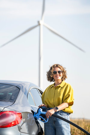 Woman holds a hydrogen fueling nozzle. Refueling car with hydrogen fuel. Wind turbines in the...