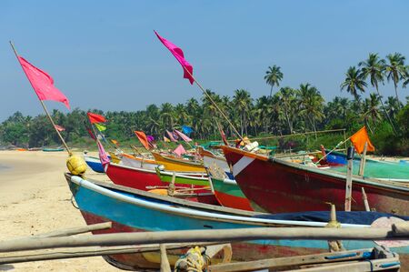 Small fishing boats in reggae colors on ocean beach seashore against blue sky. India, Goa, Maharashtraの写真素材