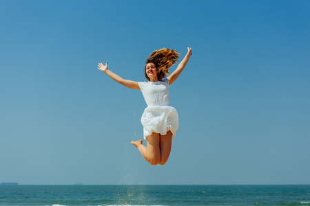 Beautiful Joyfull Girl with Long Hairs Jumping on The Beach. Vacation and Relaxingの写真素材