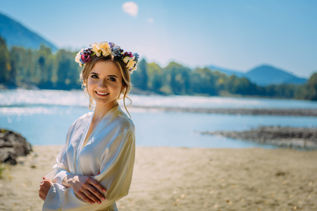 Beautiful woman wearing white dress and circlet of flowers in wild nature near riverの写真素材
