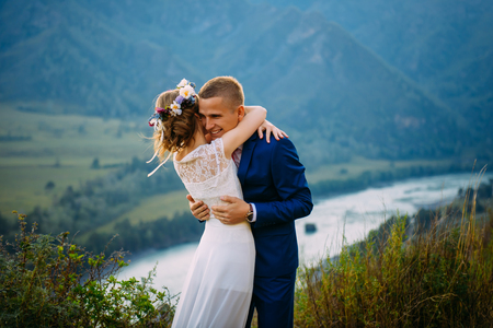 Happy newlywed couple hugging on top of the rock with background of mountainsの写真素材
