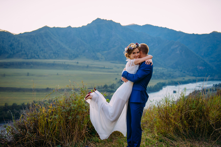 Young newly wed couple, bride and groom kissing, hugging on perfect view of mountains, blue skyの写真素材