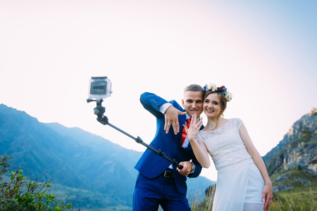 Beautiful young wedding couple making selfie and kissing on the background of mountainsの写真素材