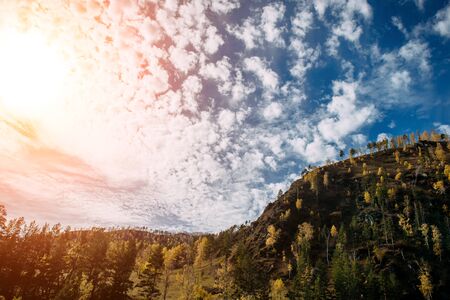 Picturesque landscape of the mountains glowing under sunlight. Fantastic sun rays with blue cloudy sky over the mountain covered with yellow trees. Breathtaking nature image.の写真素材