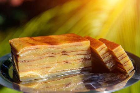 Bebinca, traditional Goan dessert from coconut milk dough, sweet Indian pudding on a metal plate, close up. Goan-Portuguese pie, delicious pieces in sunlight against palm leaves.の写真素材