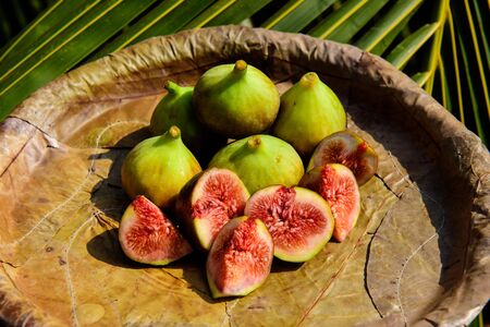 Ripe figs on a plate from leaves close up. Fresh tropical fruits: sweet sliced figs.の写真素材