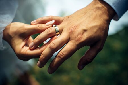 Young bride put a gold wedding ring on the groom's finger, close-up. Wedding ceremony, exchange of rings. On the hand of man wearing a wedding ring.の写真素材